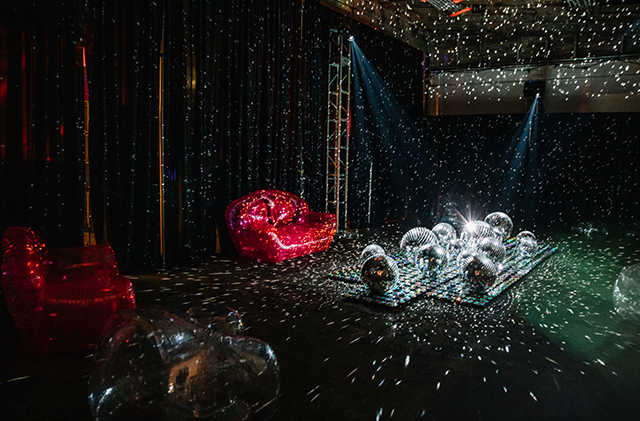 The photo shows a large room filled with CDs, mirror balls, and projection mapping creating a room filled with shimmering mirror reflections that look like the night sky.